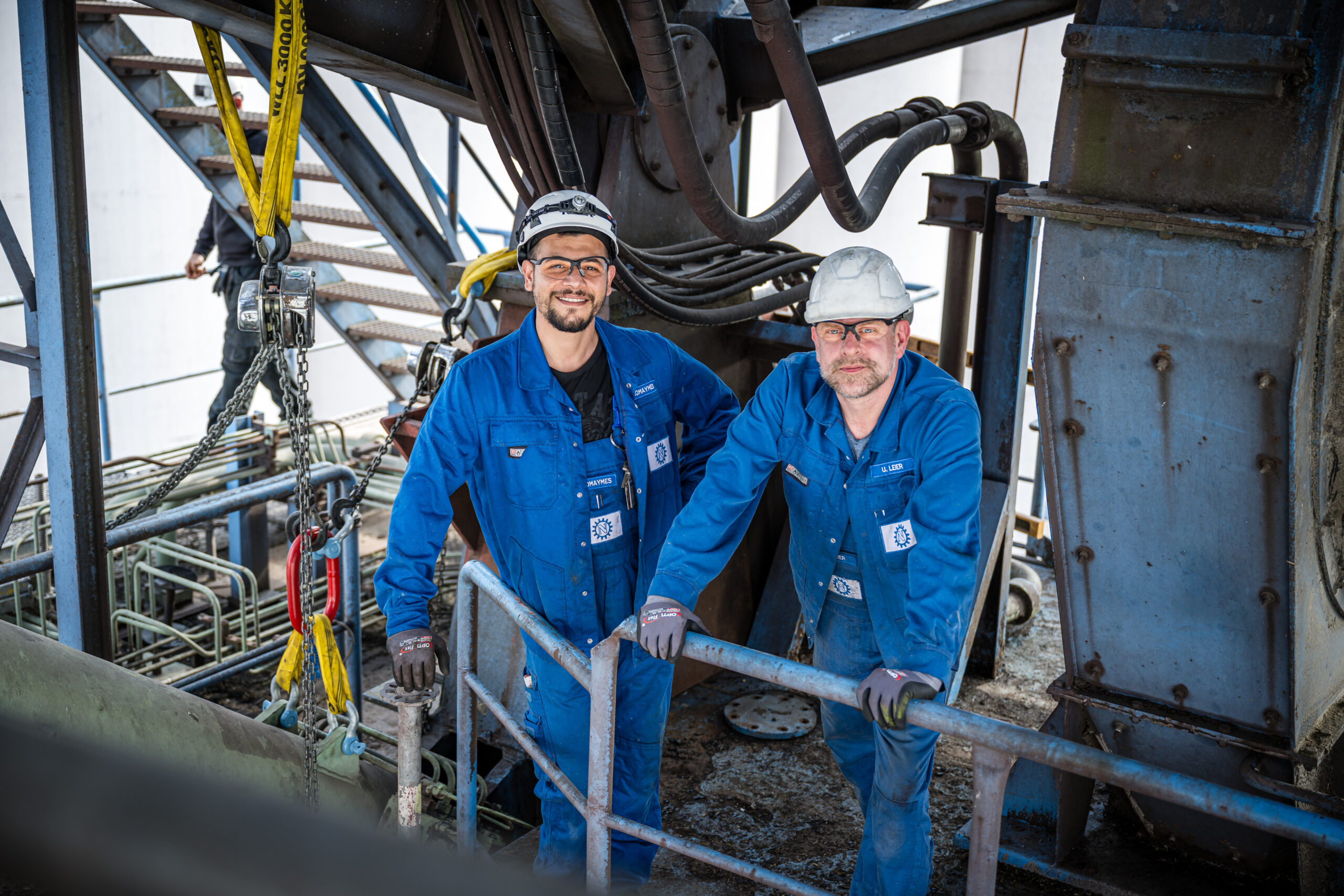 Zwei Mitarbeiter in blauer Arbeitskleidung mit Schutzhelmen im Industrieumfeld