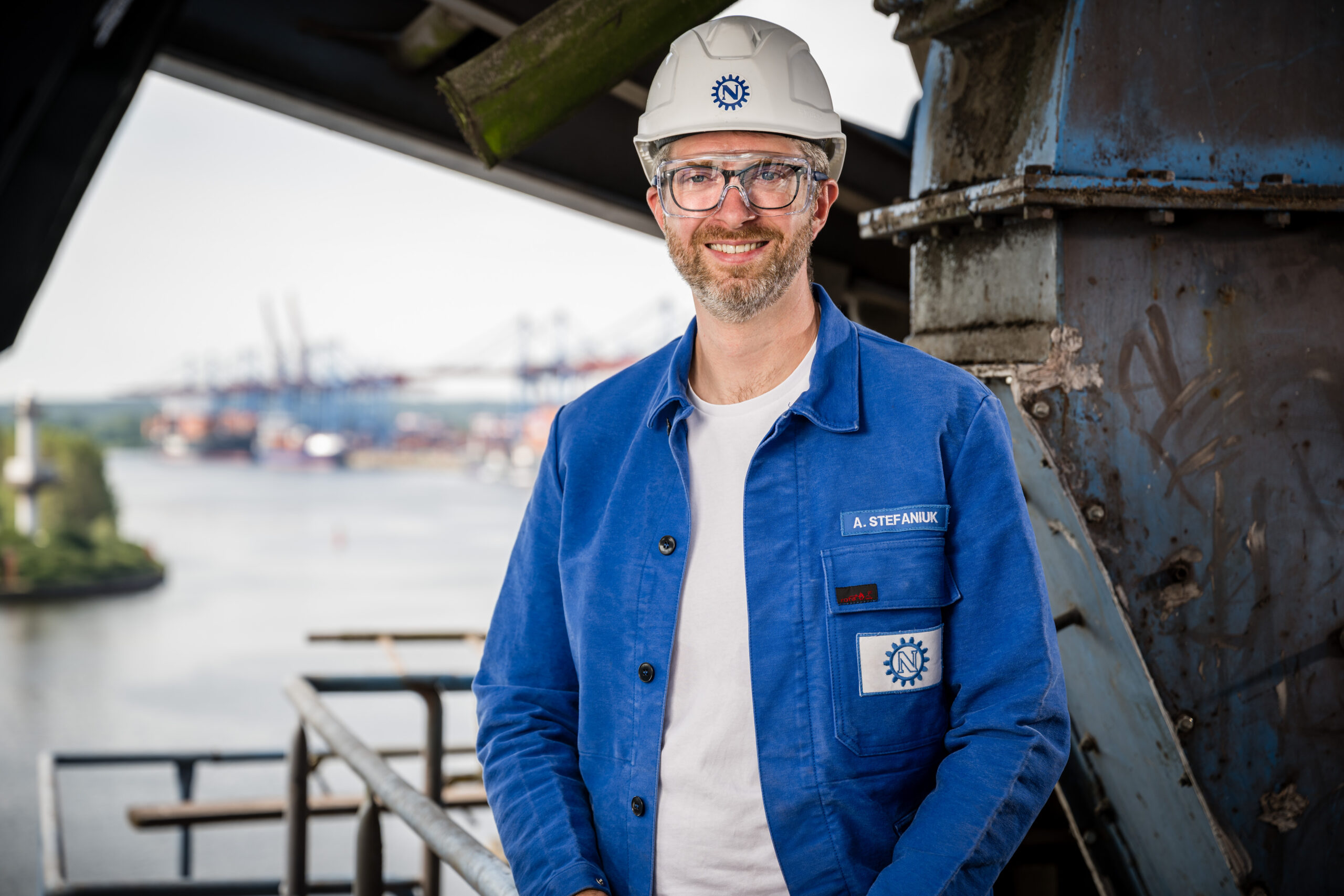 Mitarbeiter mit Helm und Schutzbrille vor Industriehafen