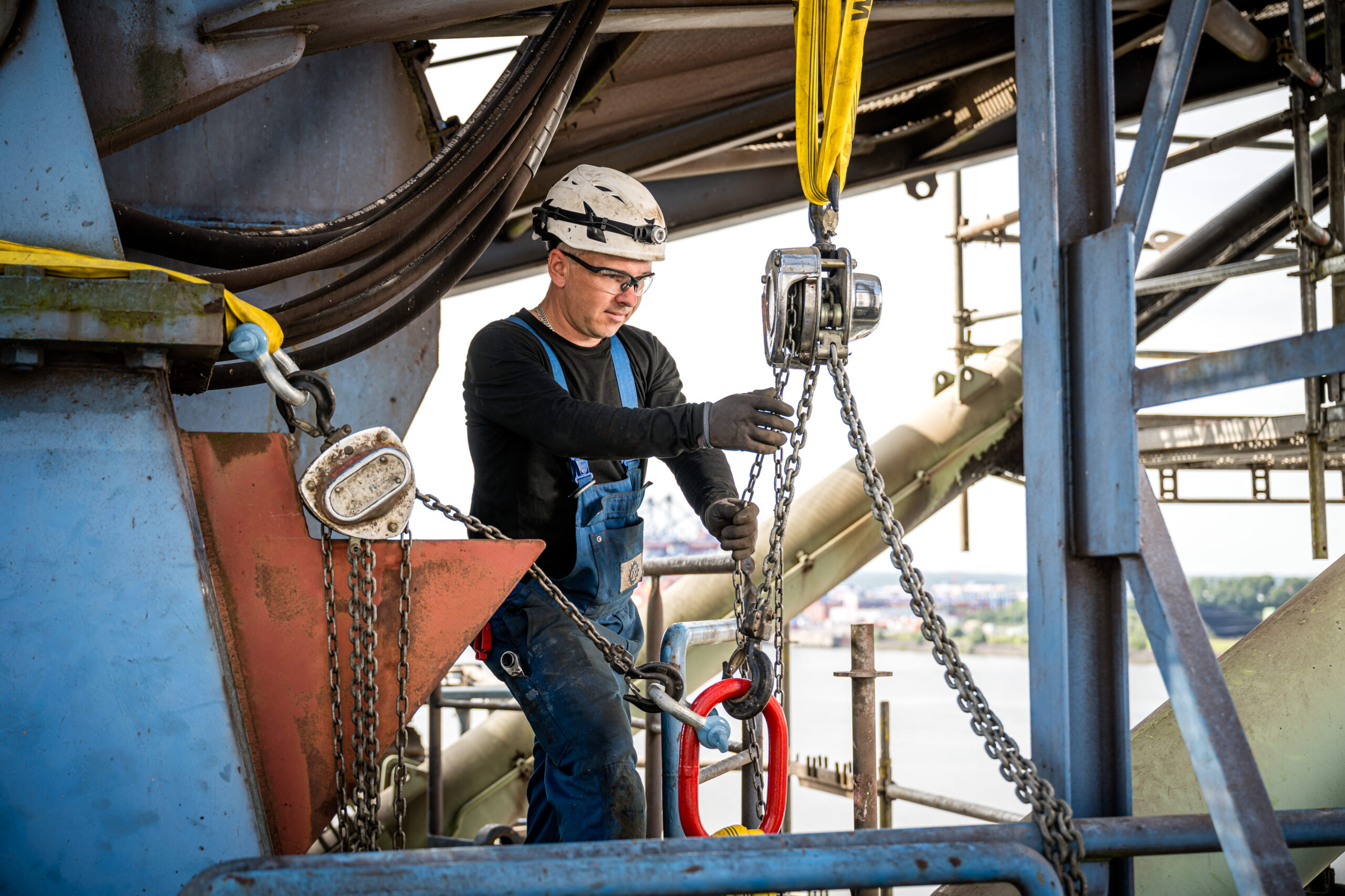 Arbeiter sichert Bauteil mit Kettenzug an Industrieanlage
