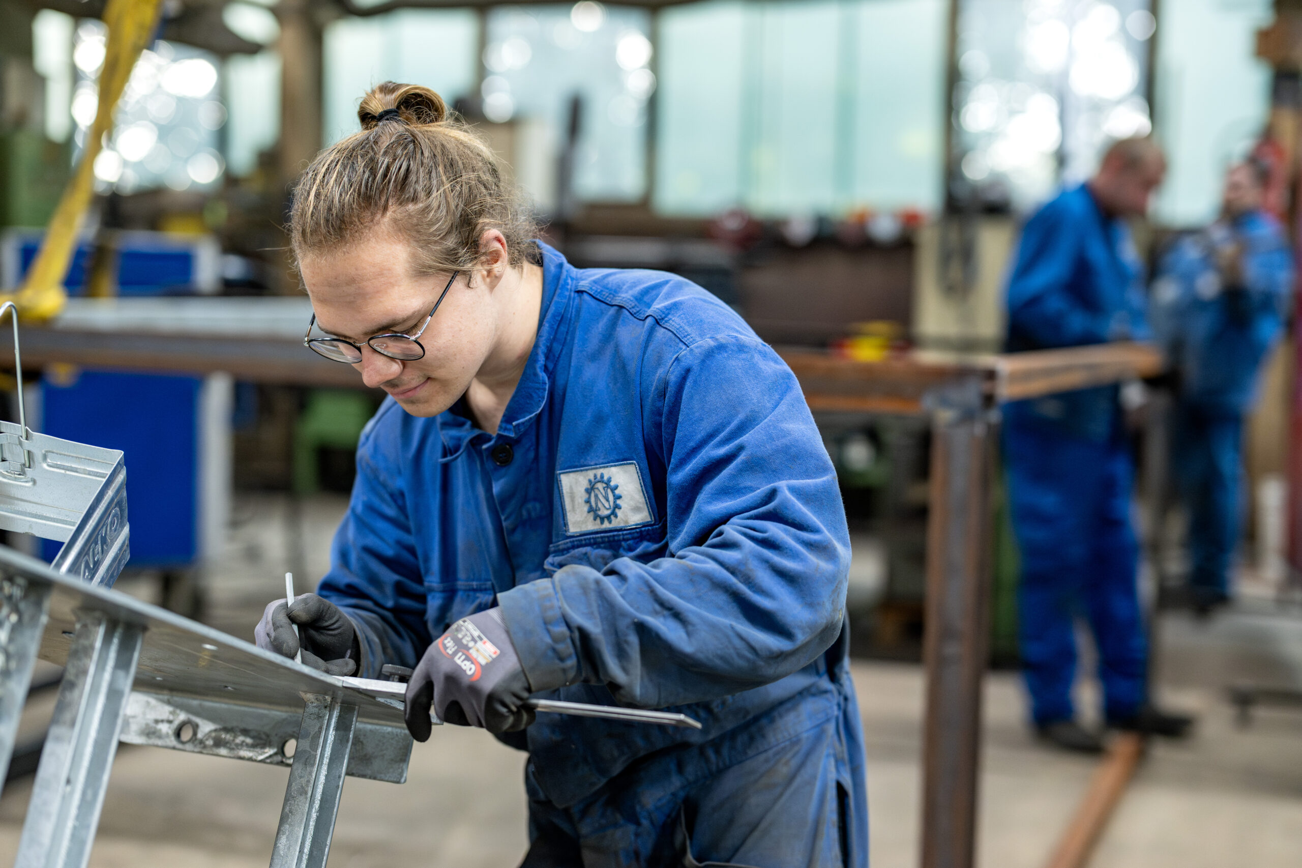Junger Mitarbeiter in blauer Arbeitskleidung markiert konzentriert ein Metallteil in der Werkstatt