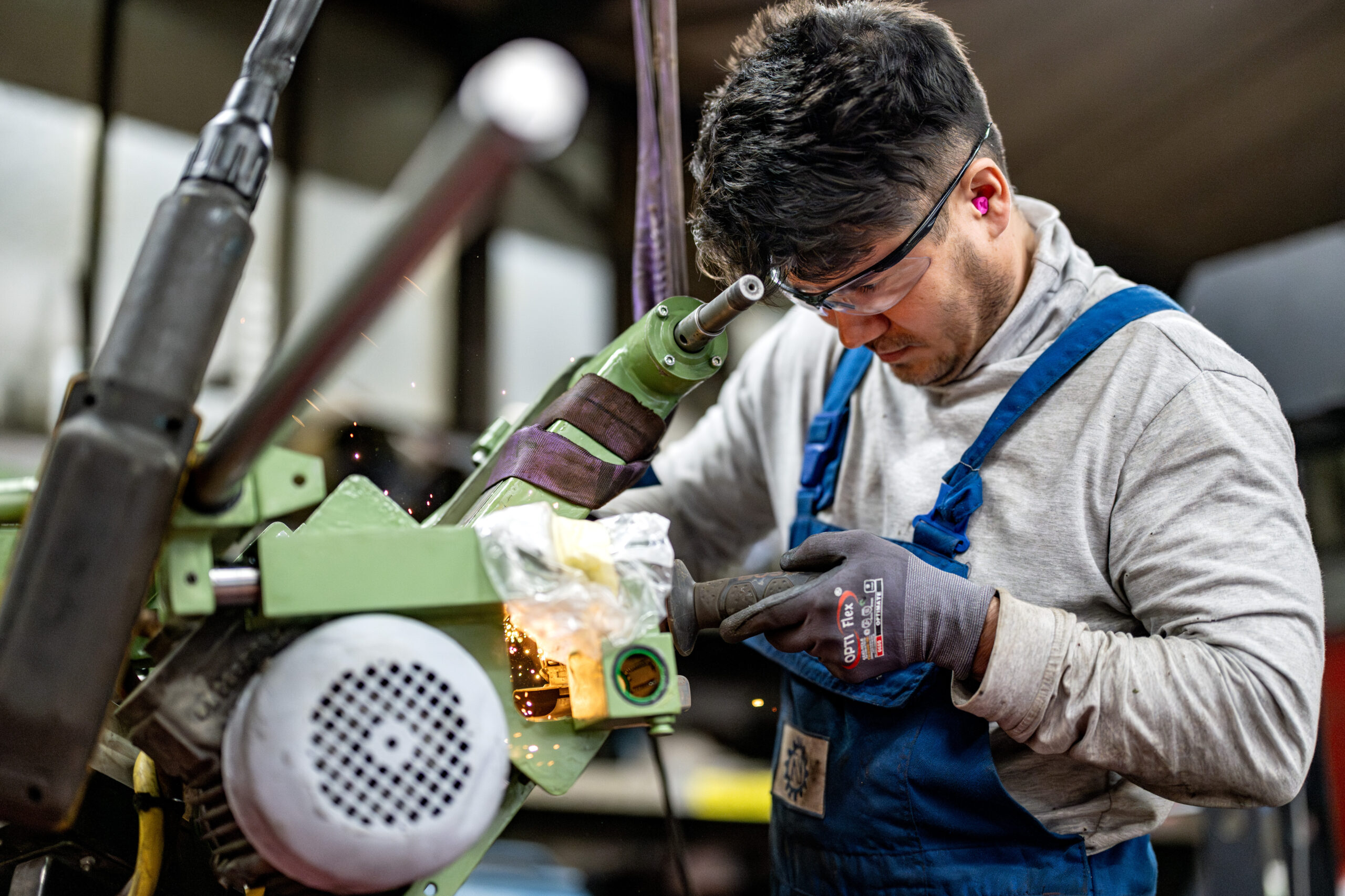 Mitarbeiter in blauer Arbeitskleidung arbeitet konzentriert mit einer Maschine, Funken fliegen während der Metallbearbeitung