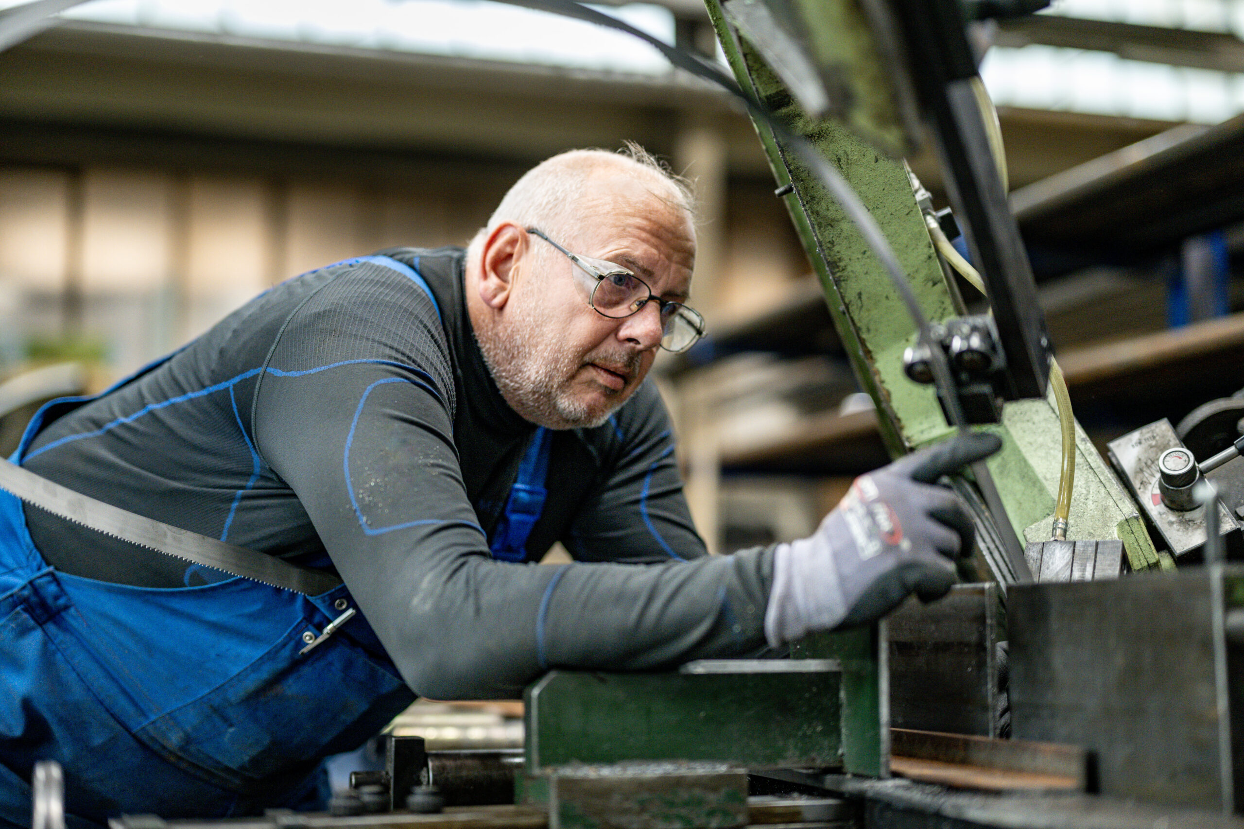 Mitarbeiter in blauer Arbeitskleidung und Schutzbrille bedient konzentriert eine Maschine