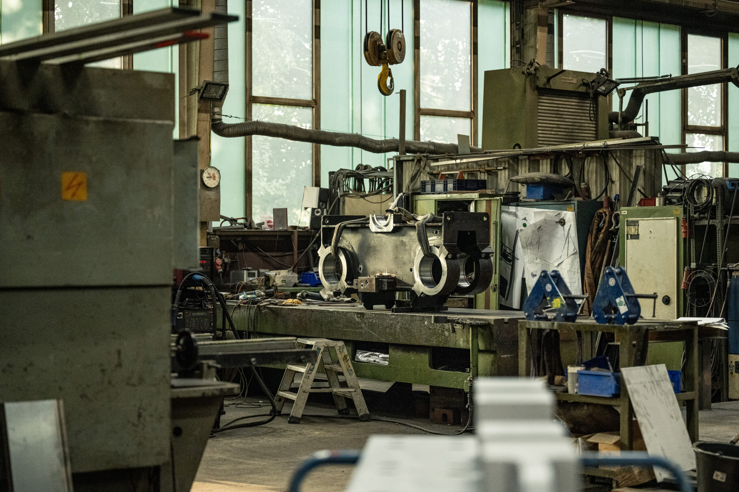 Großes Metallbauteil liegt auf einer Werkbank in einer Werkhalle, umgeben von Maschinen und Werkzeugen