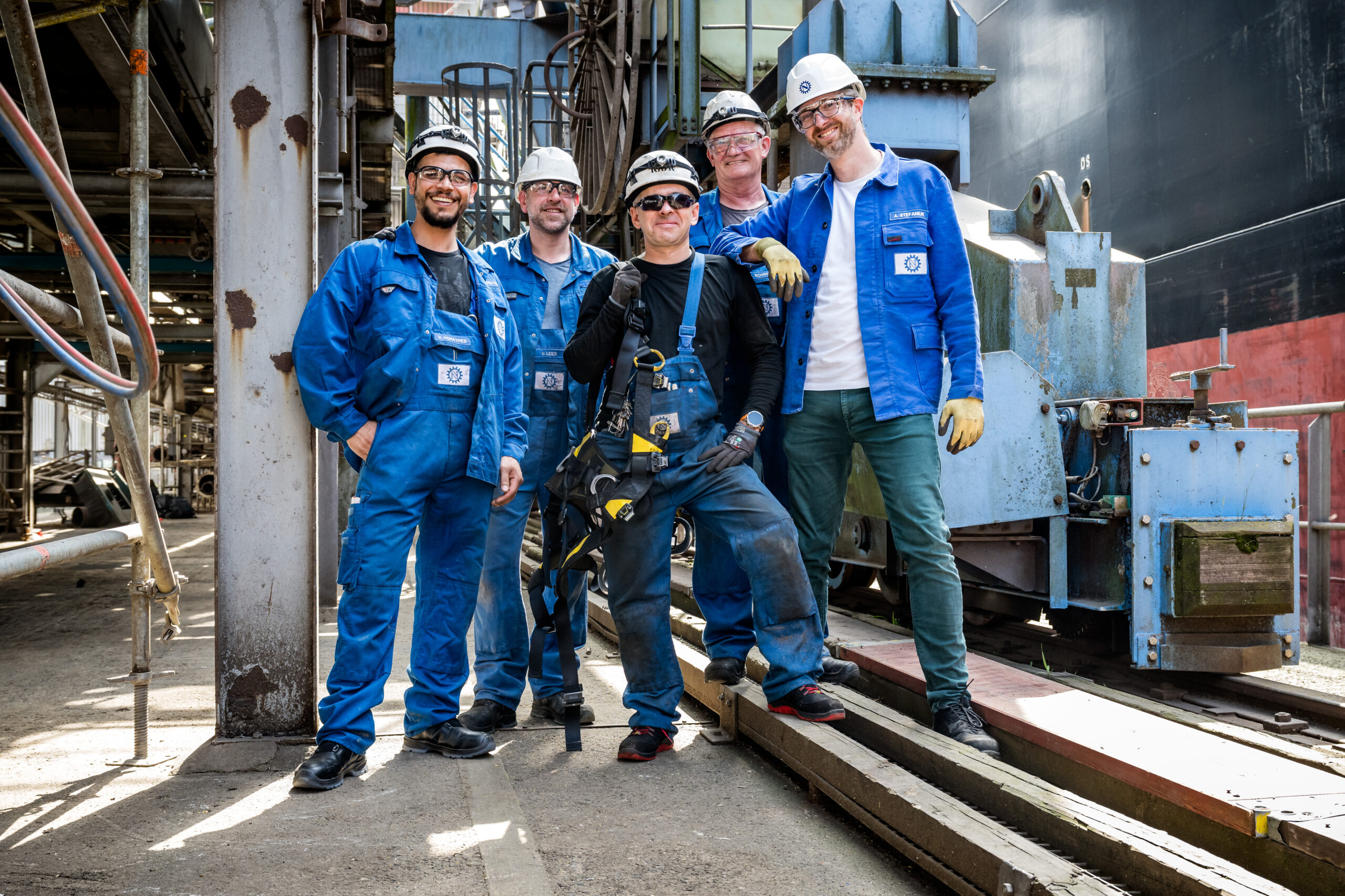 Team von fünf Mitarbeitern mit Schutzhelmen vor einer Industrieanlage