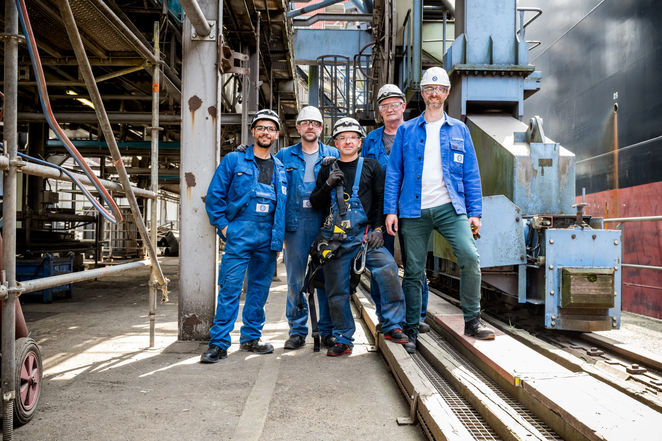 Team von fünf Mitarbeitern mit Schutzhelmen vor einer Industrieanlage