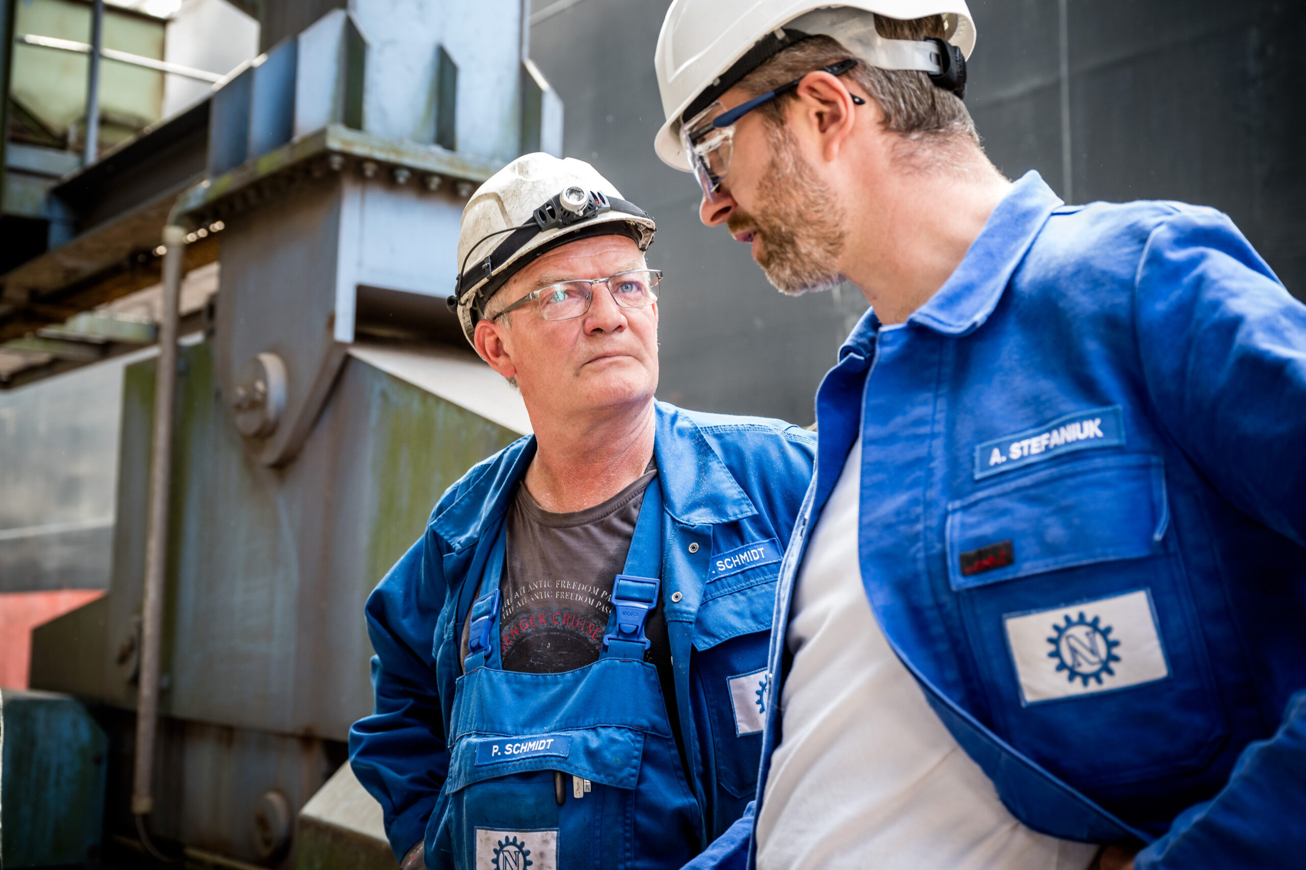 Zwei Mitarbeiter mit Schutzhelmen im intensiven Gespräch in einer Industrieanlage