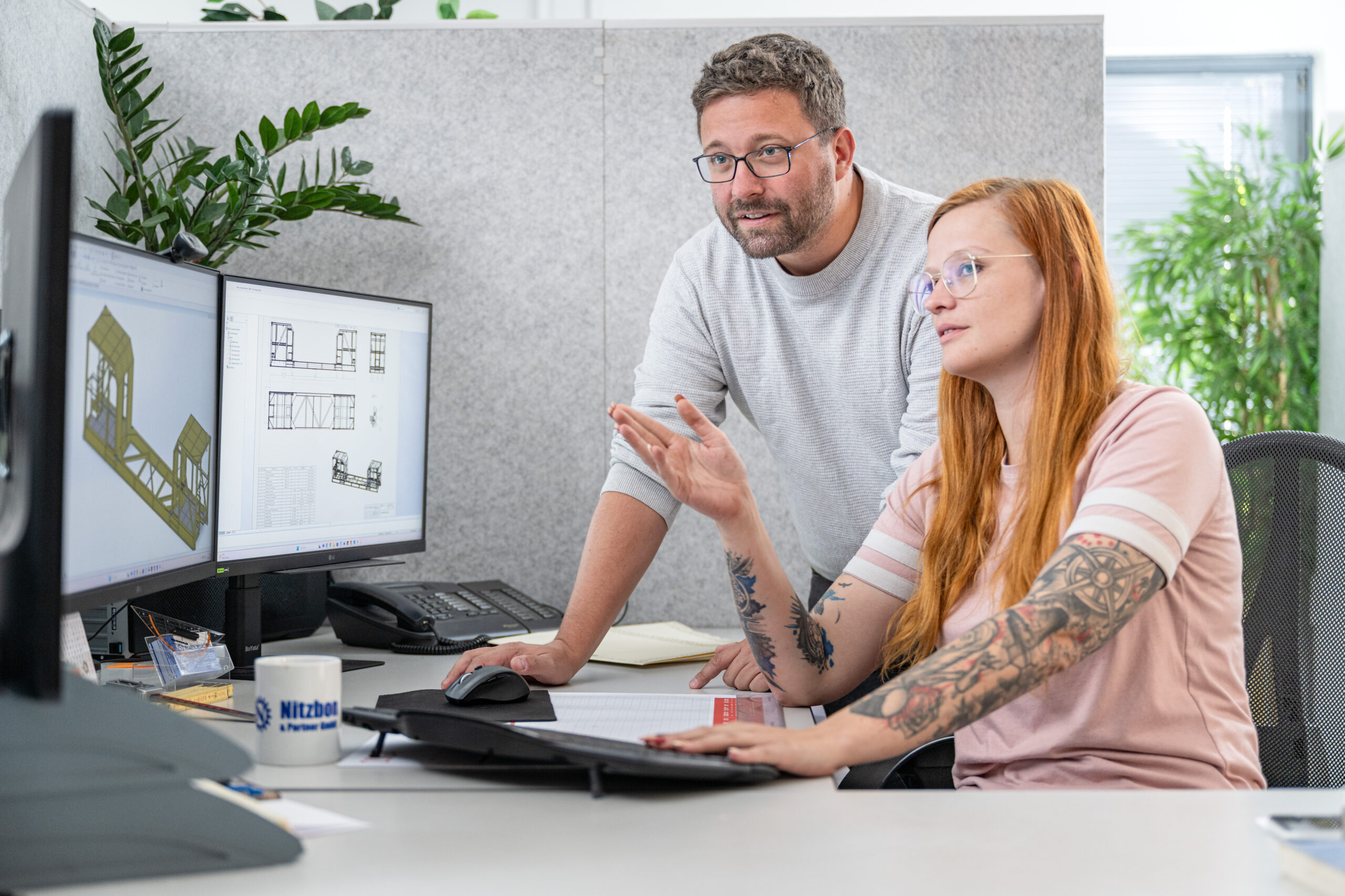 Zwei Mitarbeiter im Büro arbeiten gemeinsam am Computer an 3D-Konstruktionsplänen