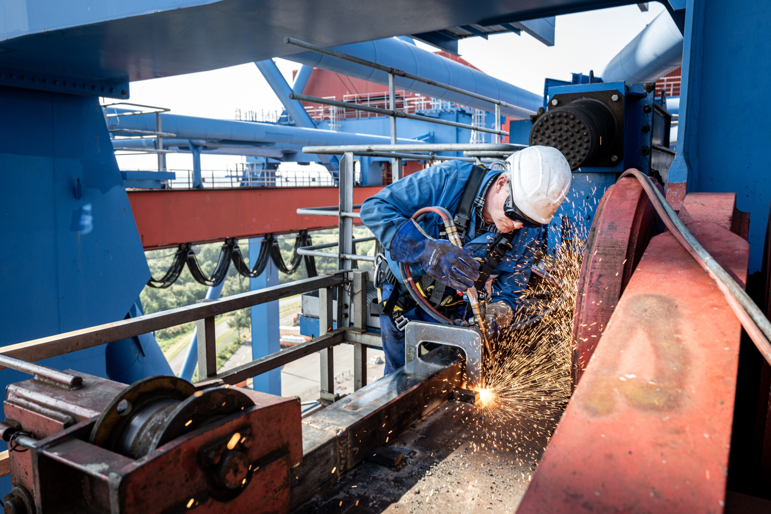 Arbeiter mit Schutzkleidung und Helm schweißt an einer Stahlkonstruktion, Funken sprühen während der Arbeit