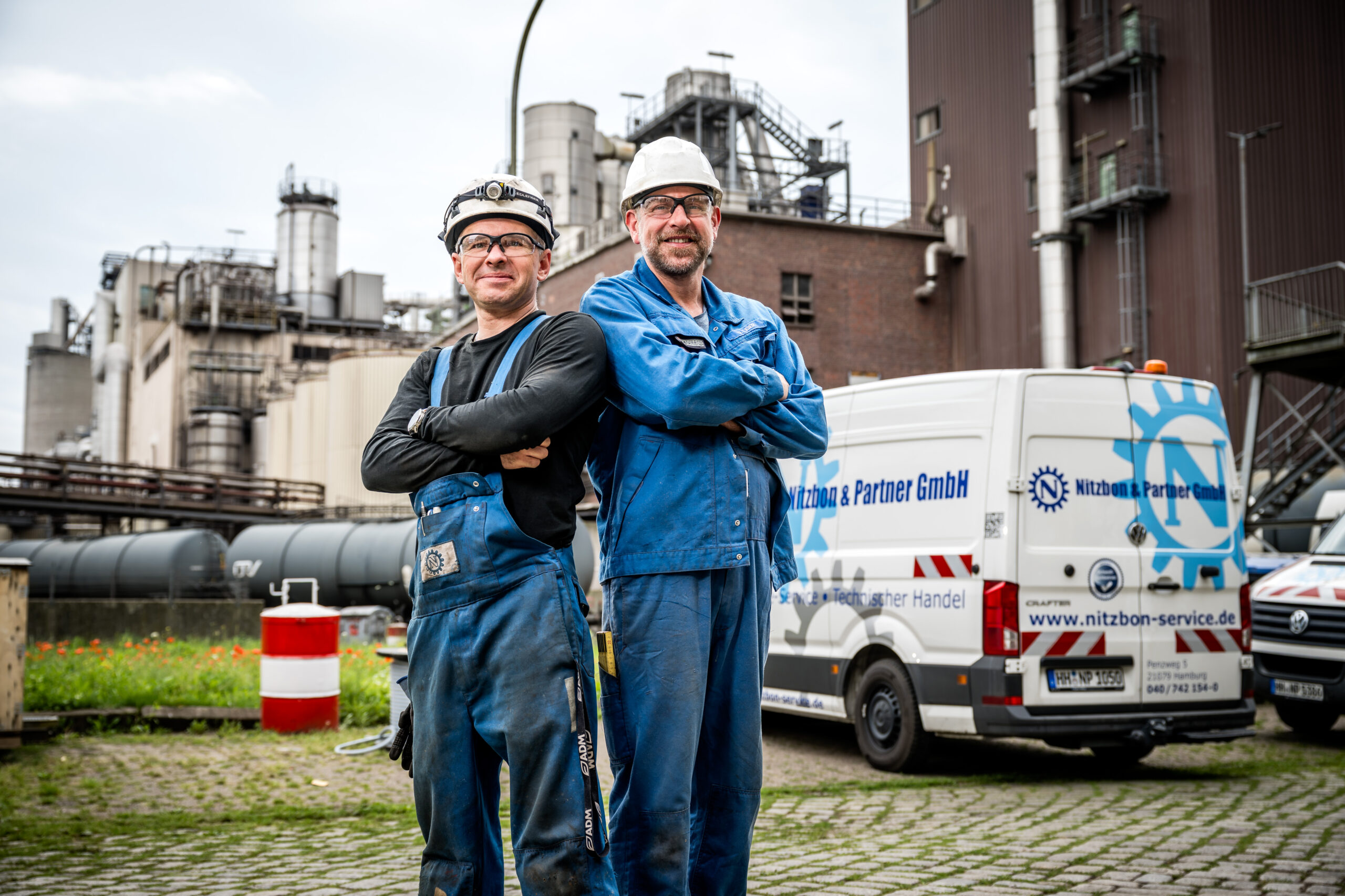 Zwei Mitarbeiter in blauer Arbeitskleidung mit Werkzeugtaschen gehen vor Service-Fahrzeugen von Nitzbon & Partner GmbH