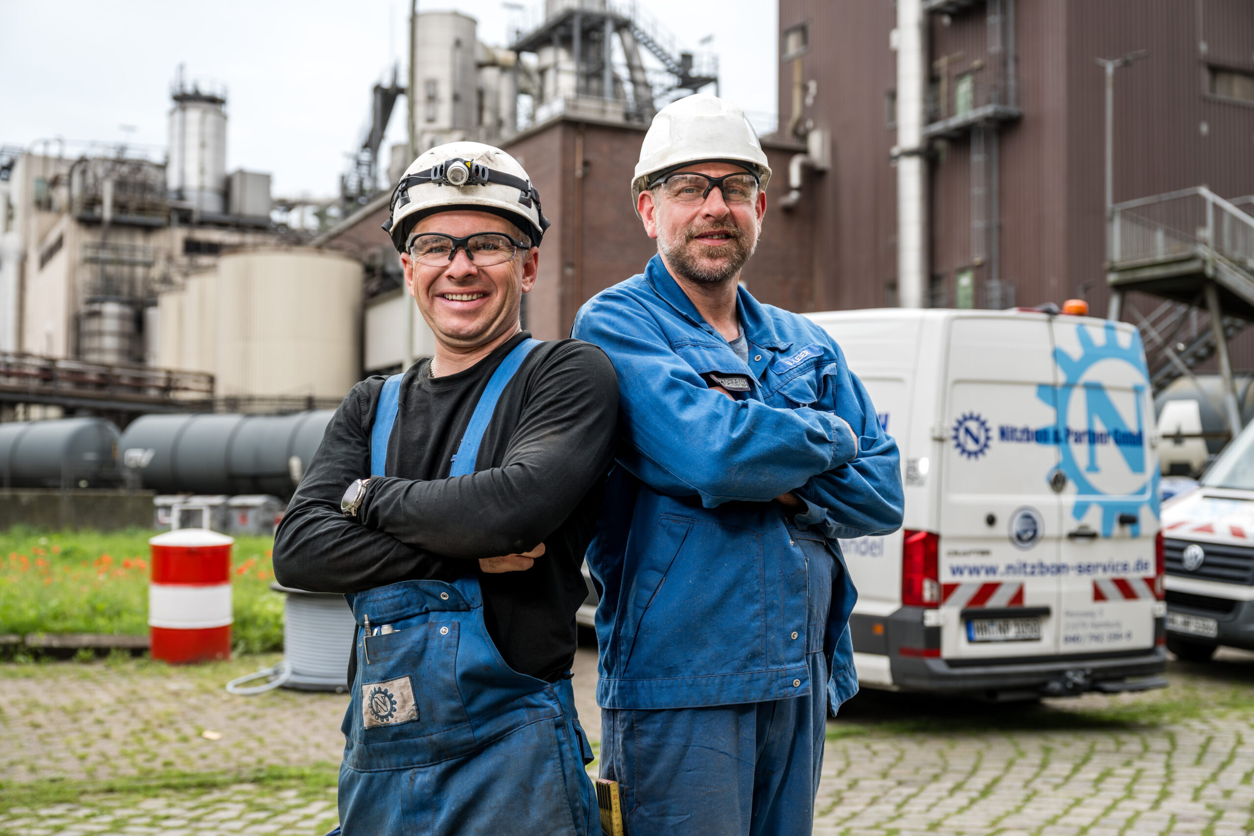 Zwei Mitarbeiter in blauer Arbeitskleidung mit Werkzeugtaschen gehen vor Service-Fahrzeugen von Nitzbon & Partner GmbH
